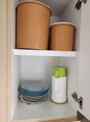 A cabinet with two terracotta pots on the top shelf and a stack of blue plates on the bottom shelf.