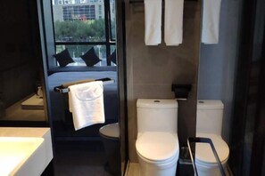 A modern bathroom with a shower, two toilets, and a bed with a view.
