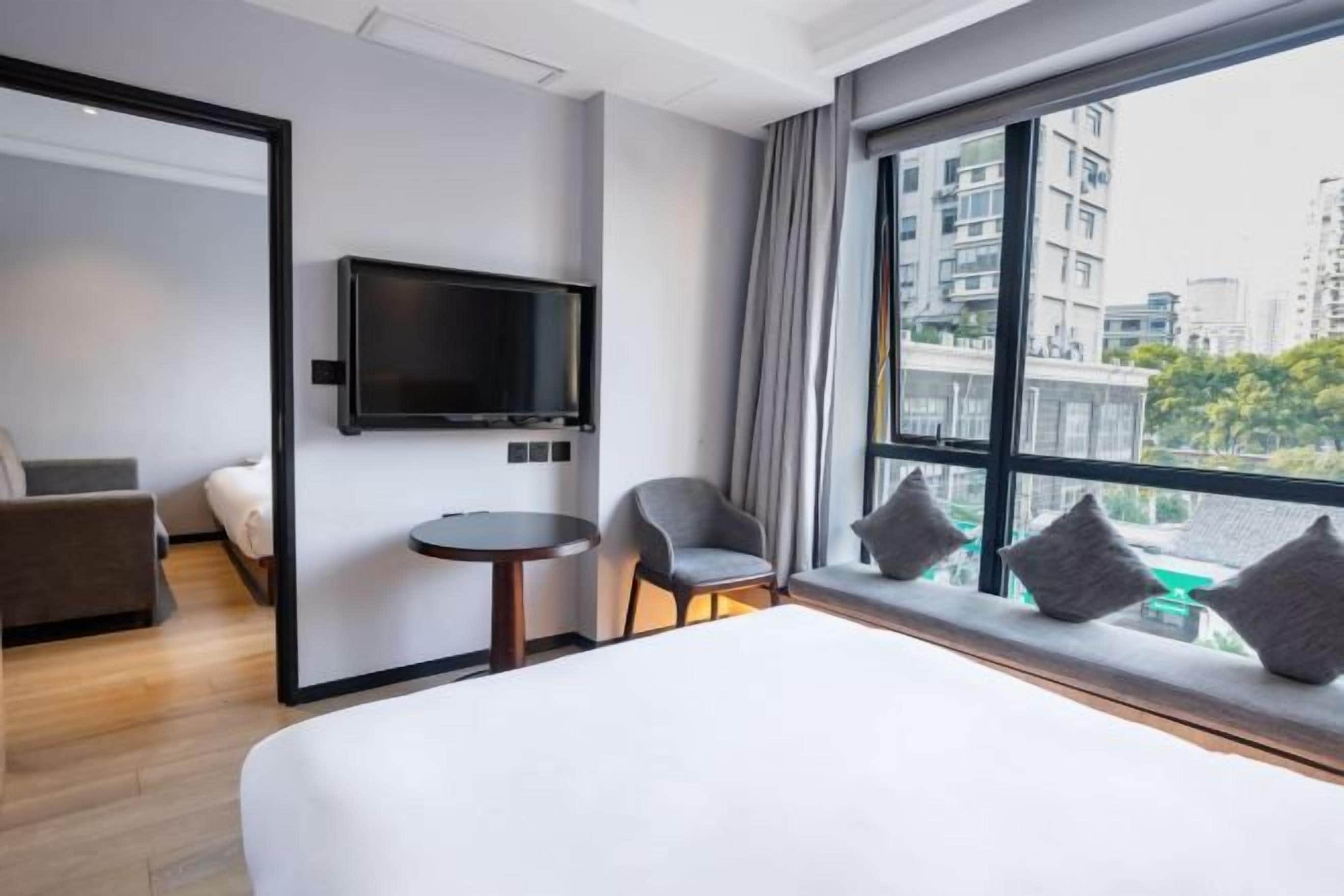 A hotel room with a bed, a TV, a small table, two chairs, and a window with a city view.
