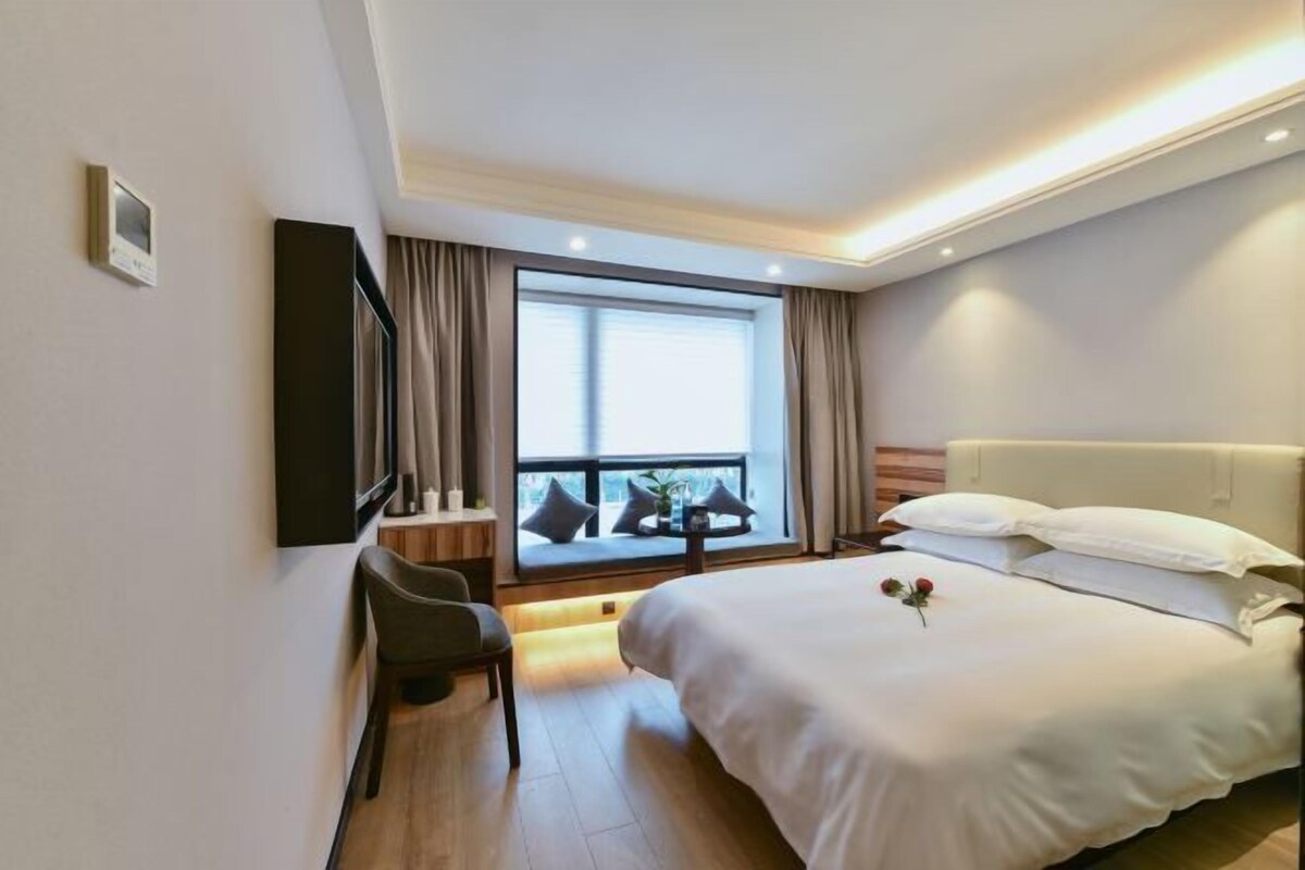 A hotel room with a large bed, a desk, a chair, and a window with curtains.