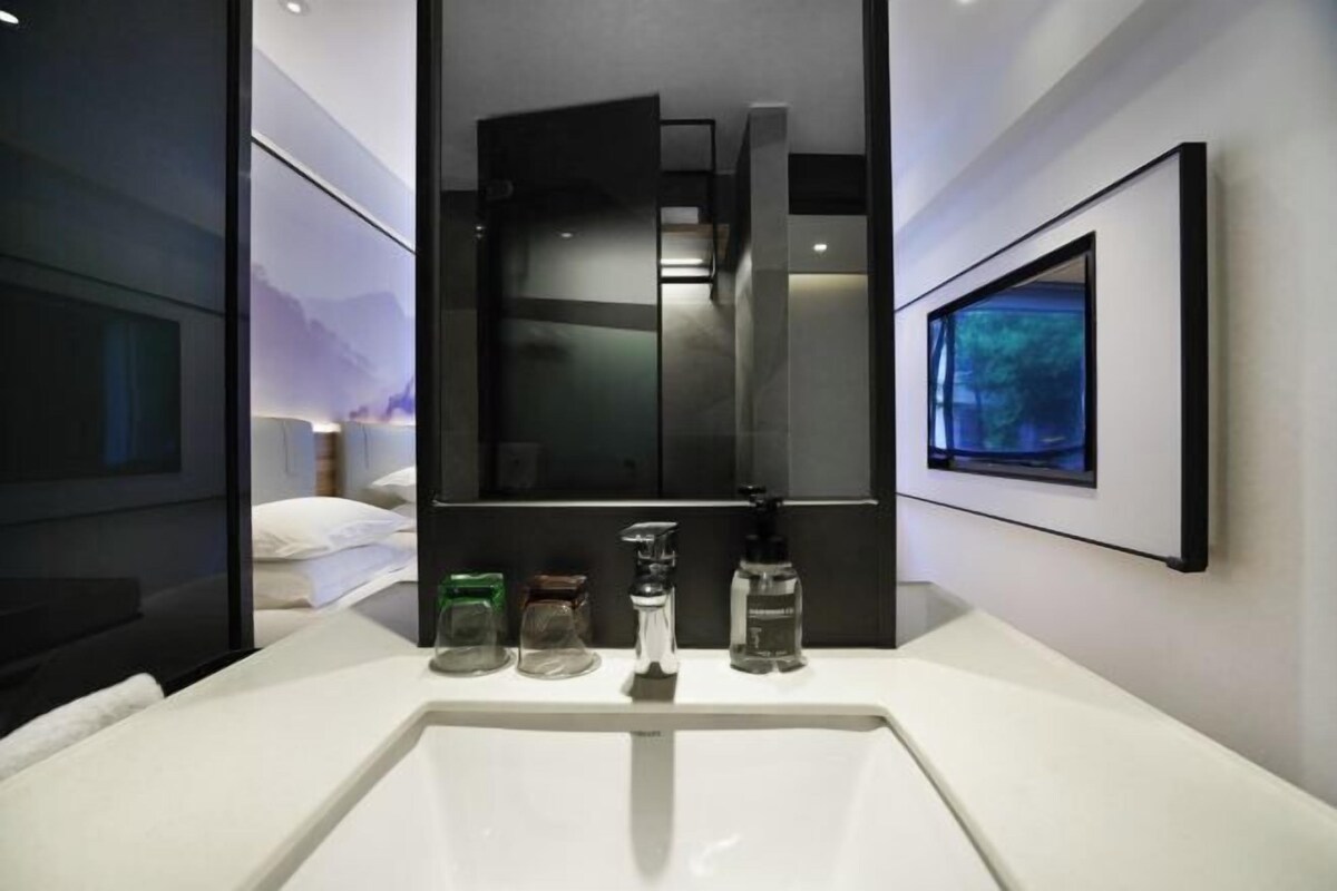 A modern bathroom with a large mirror, a white sink, and a framed picture on the wall.