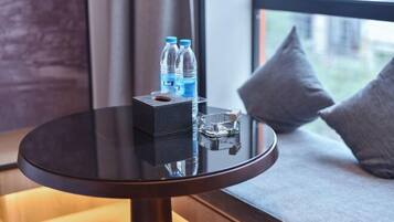 A round table with a black surface, two water bottles, a glass, and a box, placed on a window seat with a view of buildings.