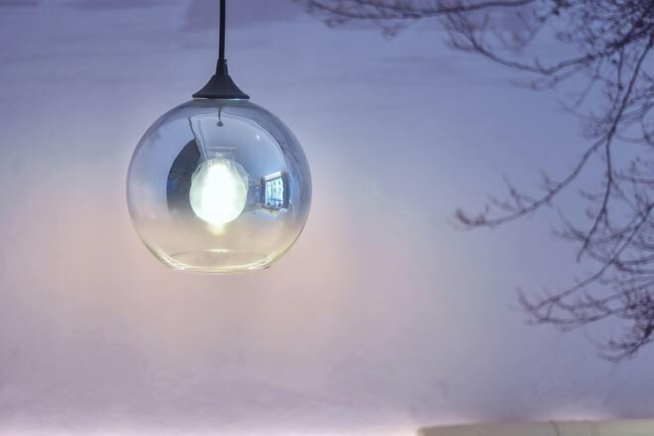 Una lámpara colgante esférica con cubierta de vidrio transparente, suspendida de un accesorio de techo negro.