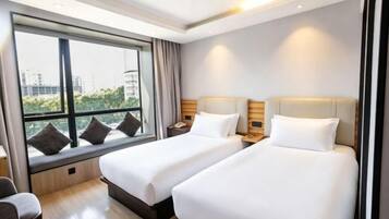 A hotel room with two beds, a window with a city view, a desk, and a chair.