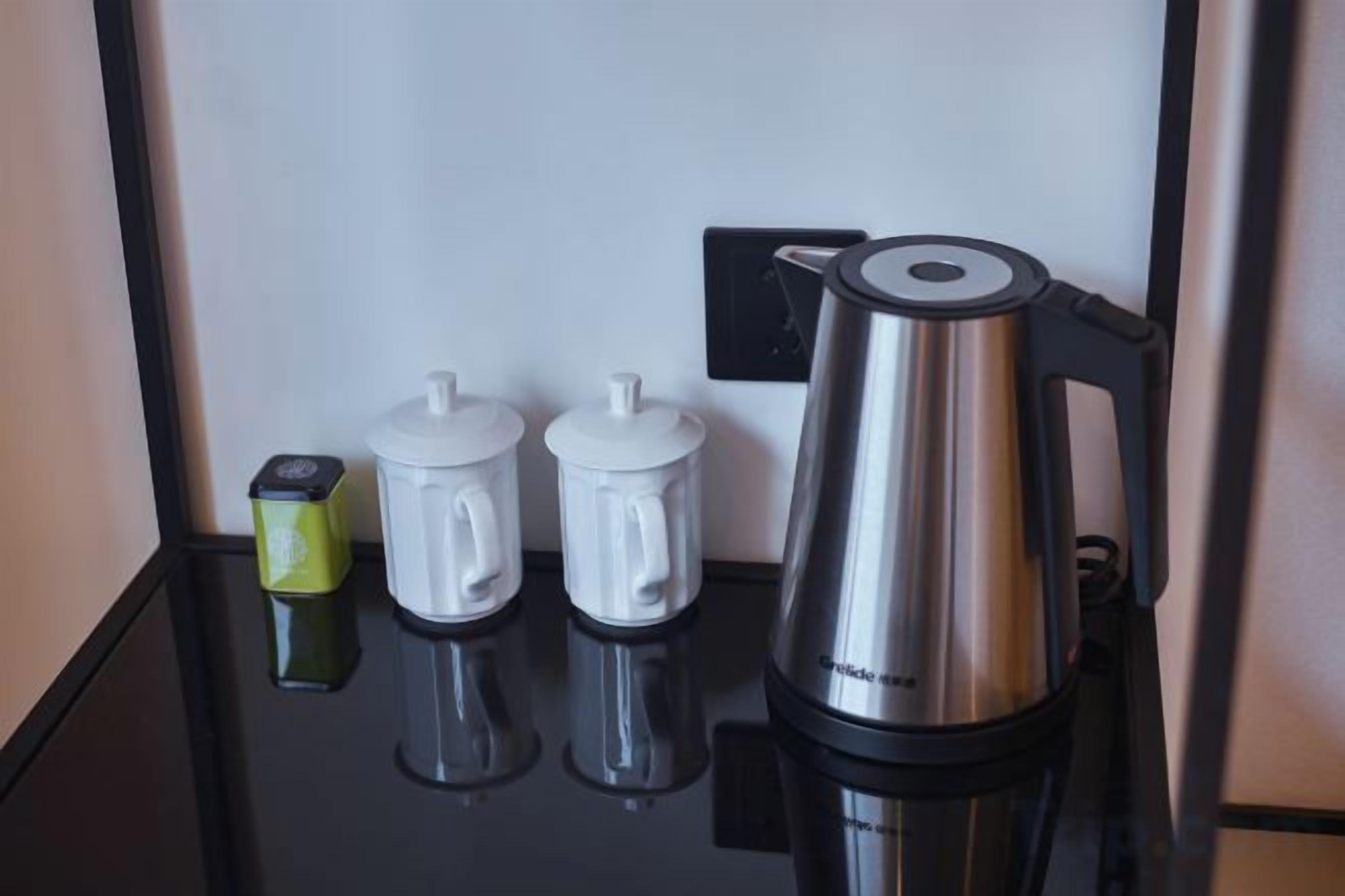 A coffee station with a coffee maker, two milk frothers, and a small electric kettle on a black countertop.