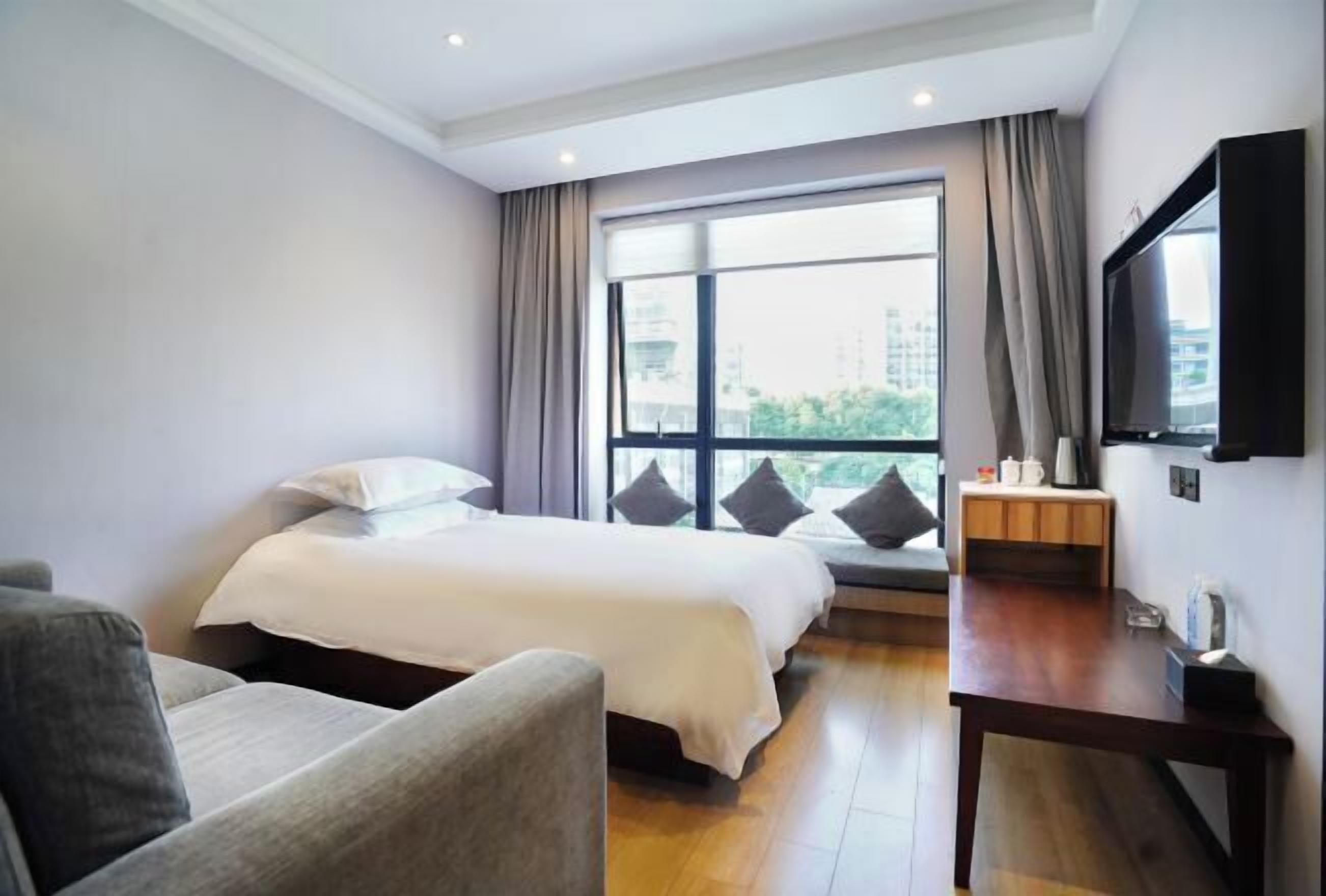 Habitación de hotel con cama, sofá, televisión, una mesita y ventana con cortinas.