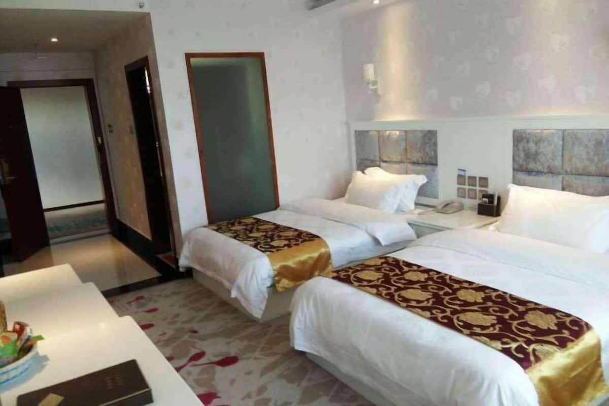 Quarto de hotel com duas camas, uma mesinha de cabeceira e uma porta.