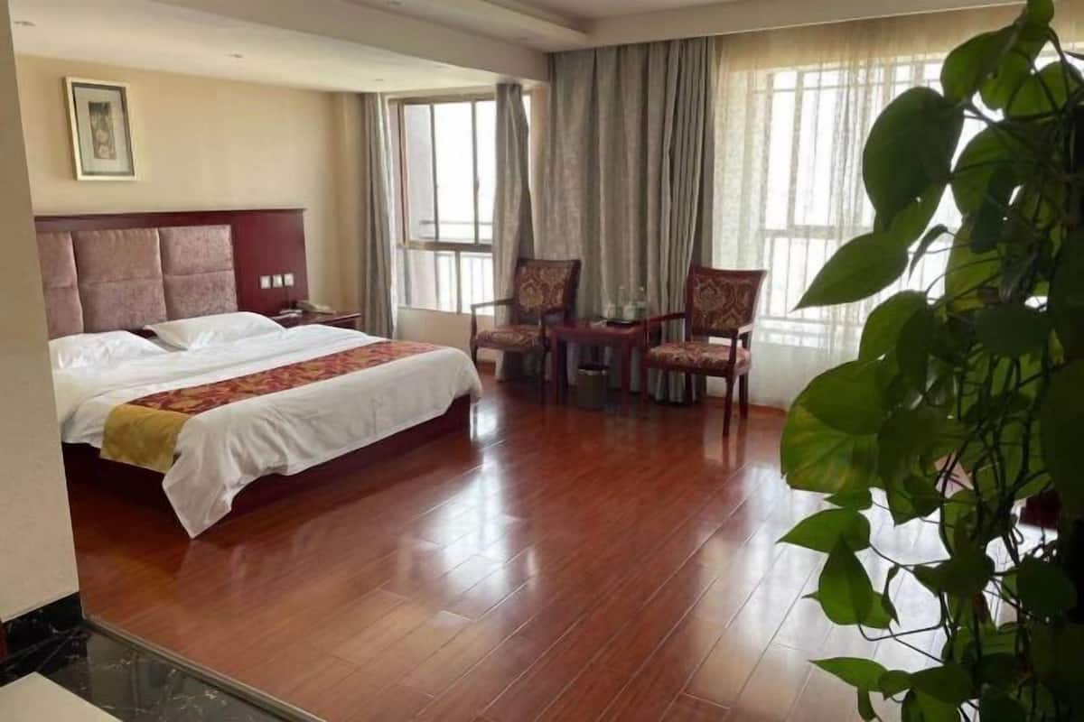 Quarto de hotel com uma cama grande, duas cadeiras, uma mesinha e uma planta.