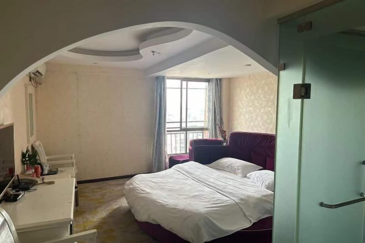 Quarto de hotel com cama, escrivaninha e janela com cortinas.