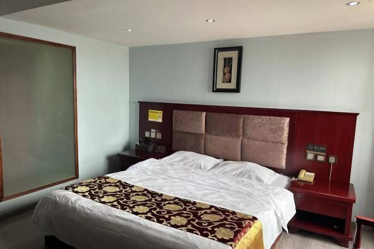 Quarto de hotel com cama, mesa de cabeceira, quadro na parede e uma janela grande.