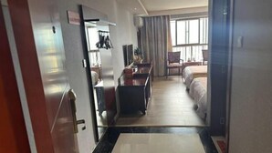 Una habitación de hotel con cama, escritorio, silla y ventana con cortinas.