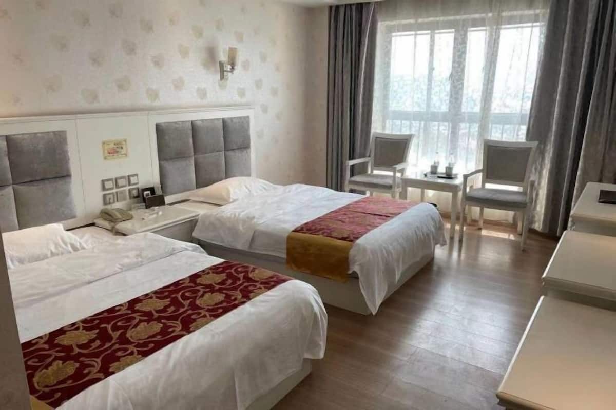 Quarto de hotel com duas camas, uma escrivaninha e uma cadeira.