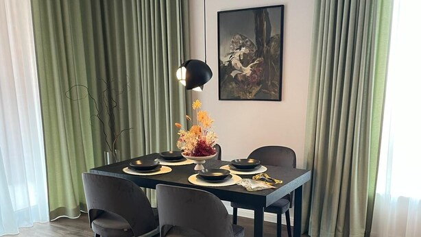 Un coin repas avec une table dressée pour quatre personnes, entourée de chaises, un vase de fleurs et un tableau accroché au mur.