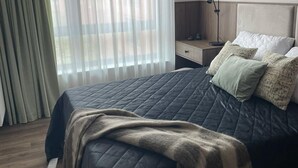 Une chambre moderne avec un grand lit, une table de chevet, une lampe et des rideaux légers.