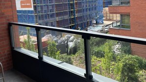 Un balcon donnant sur un immeuble en construction, un mur de briques et une fenêtre.