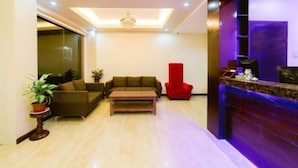 A modern living room with a sofa, a red chair, a coffee table, and a reception desk with a TV.