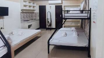 A dormitory room with bunk beds, a desk, a mirror, and a wardrobe.