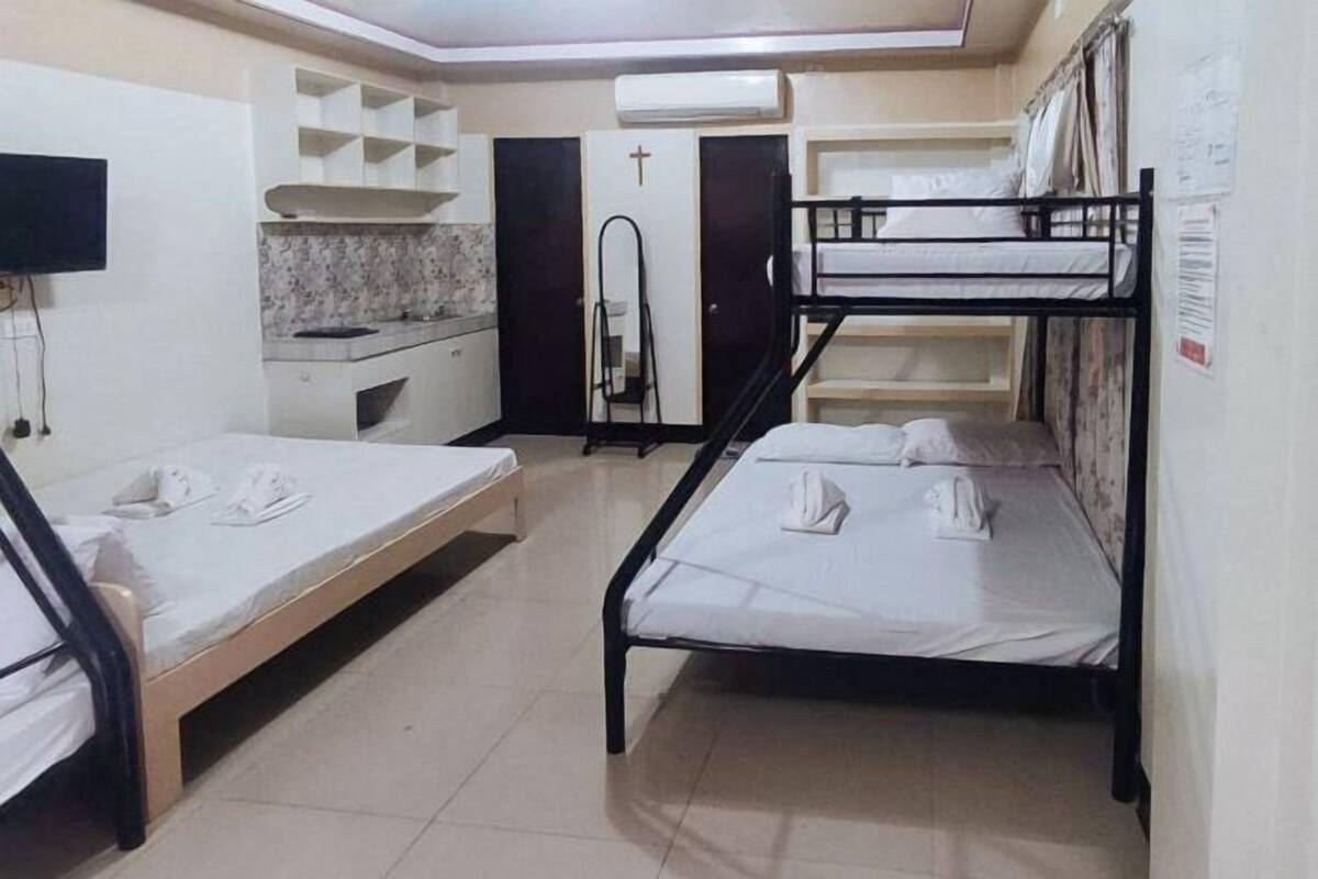 Un dormitorio con literas, televisión, kitchenette y una cruz en la puerta.