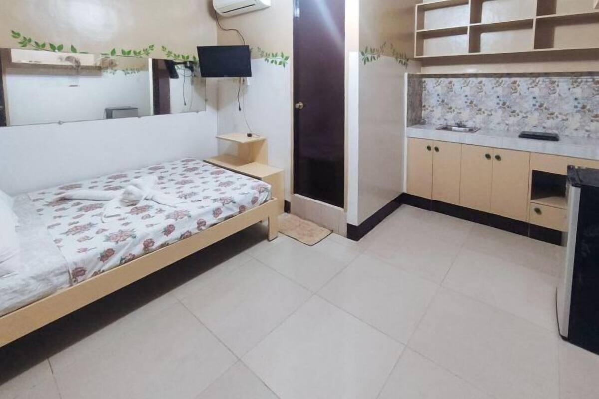 Un dormitorio con cama, televisor, escritorio pequeño y baño con ducha.