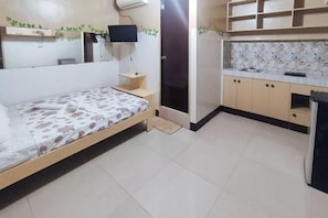 A bedroom with a bed, a TV, a small desk, and a bathroom with a shower.