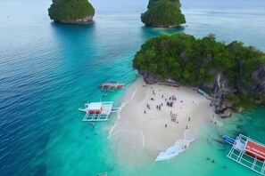 An aerial view of a beach with clear turquoise waters, a sandy shore, and several boats anchored nearby. - RedDoorz @ Isabelle Tourist Hotel Hinatuan (Hinatuan)
