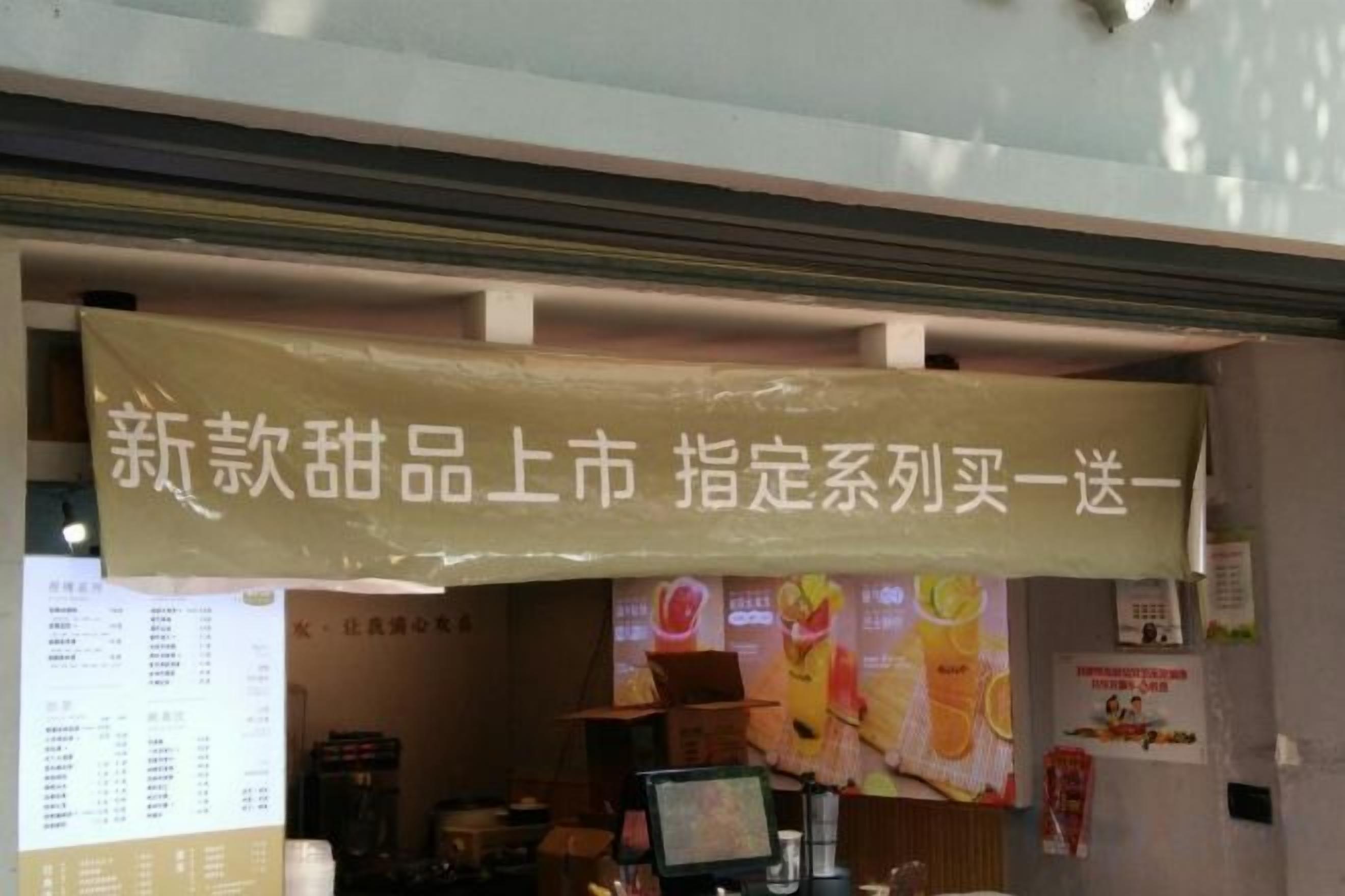 A storefront with a sign in a foreign language, a menu board, and a counter with a computer monitor.