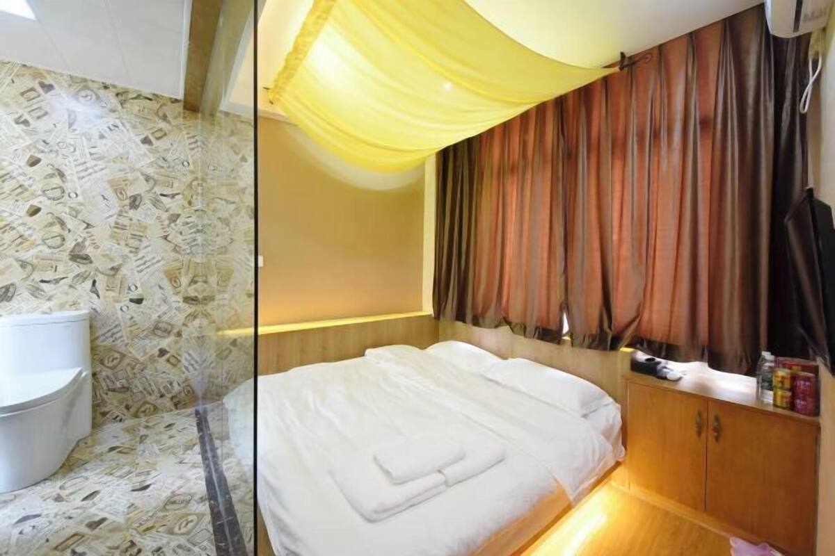 A hotel room with a bed, a wooden cabinet, a toilet, and a curtain.