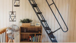 Eine Holztreppe mit einer Metallleiter, einem Ventilator und einem Bücherregal mit Büchern und einer Pflanze.