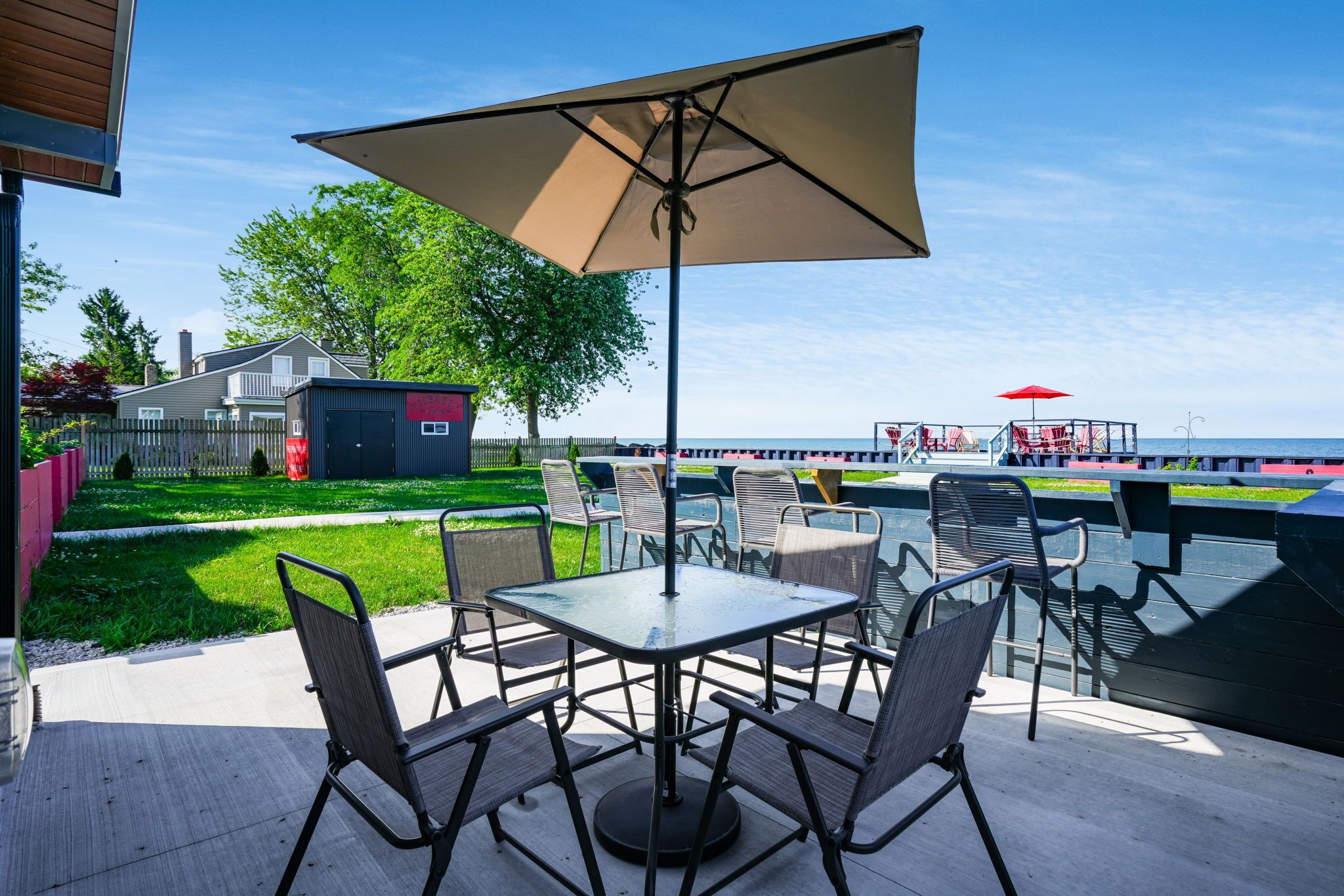 An outdoor patio with a table and chairs, a large umbrella, and a view of the sea.