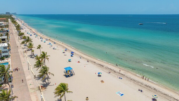 Een strand met helder turquoise water, palmbomen en strandparasols.