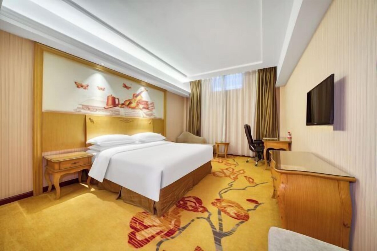 A hotel room with a bed, bedside table, chair, desk, and a television mounted on the wall.