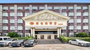 A hotel entrance with a classical facade, multiple windows, and a parking lot with cars. - Vienna Hotel (Hangzhou Xiaoshan Airport) (Hangzhou)