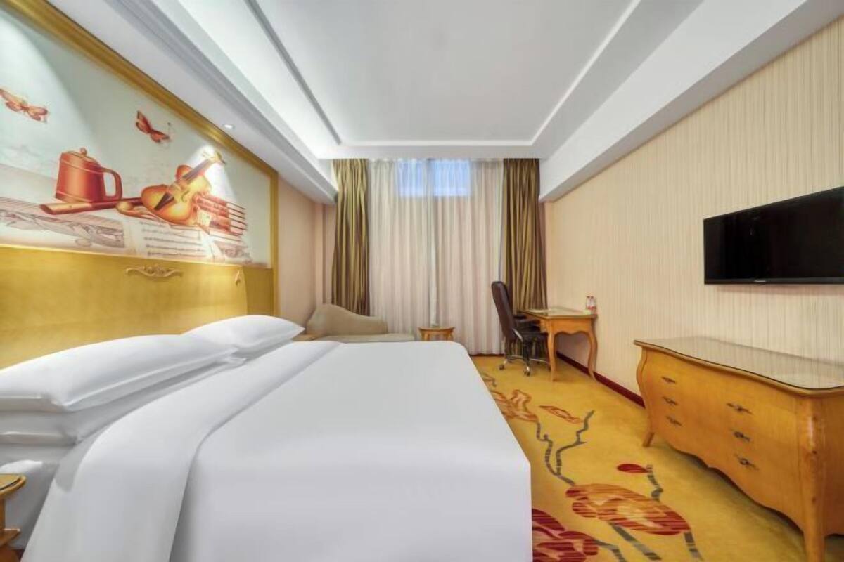 A hotel room with a bed, a desk, a chair, a television, and a window with curtains.