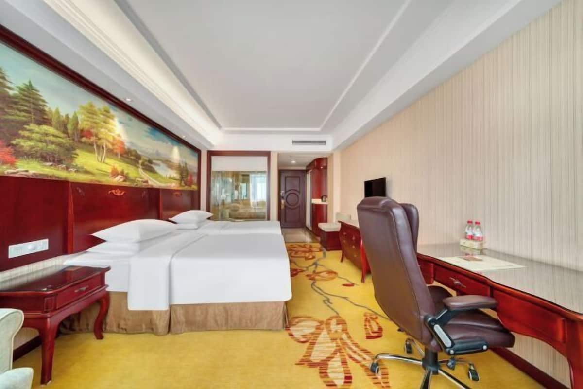 A hotel room with a bed, a desk, a chair, a television, and a painting on the wall.