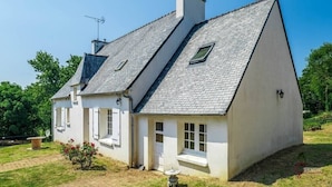 Ein zweistöckiges Haus mit einem geneigten Dach, einem Schornstein und einem kleinen Garten mit Blumen.