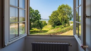Ein Zimmer mit Blick auf eine grüne Landschaft und ein Gewässer durch große Fenster.