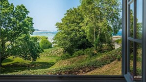 Blick aus einem Fenster auf eine üppige grüne Landschaft mit Bäumen und einem Gewässer in der Ferne.