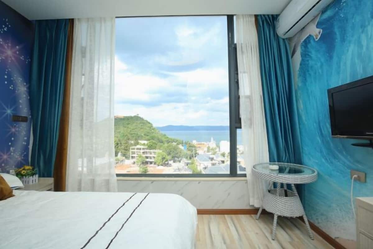 Una camera d'albergo con una grande finestra, un letto, una TV e un tavolino.