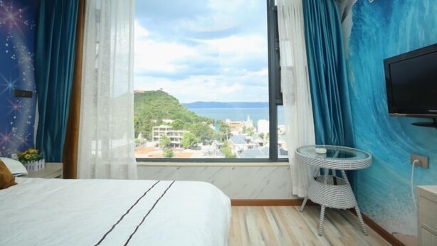 A hotel room with a large window, a bed, a TV, and a small table. - Chengjiang Green Water Hotel (Chengjiang)