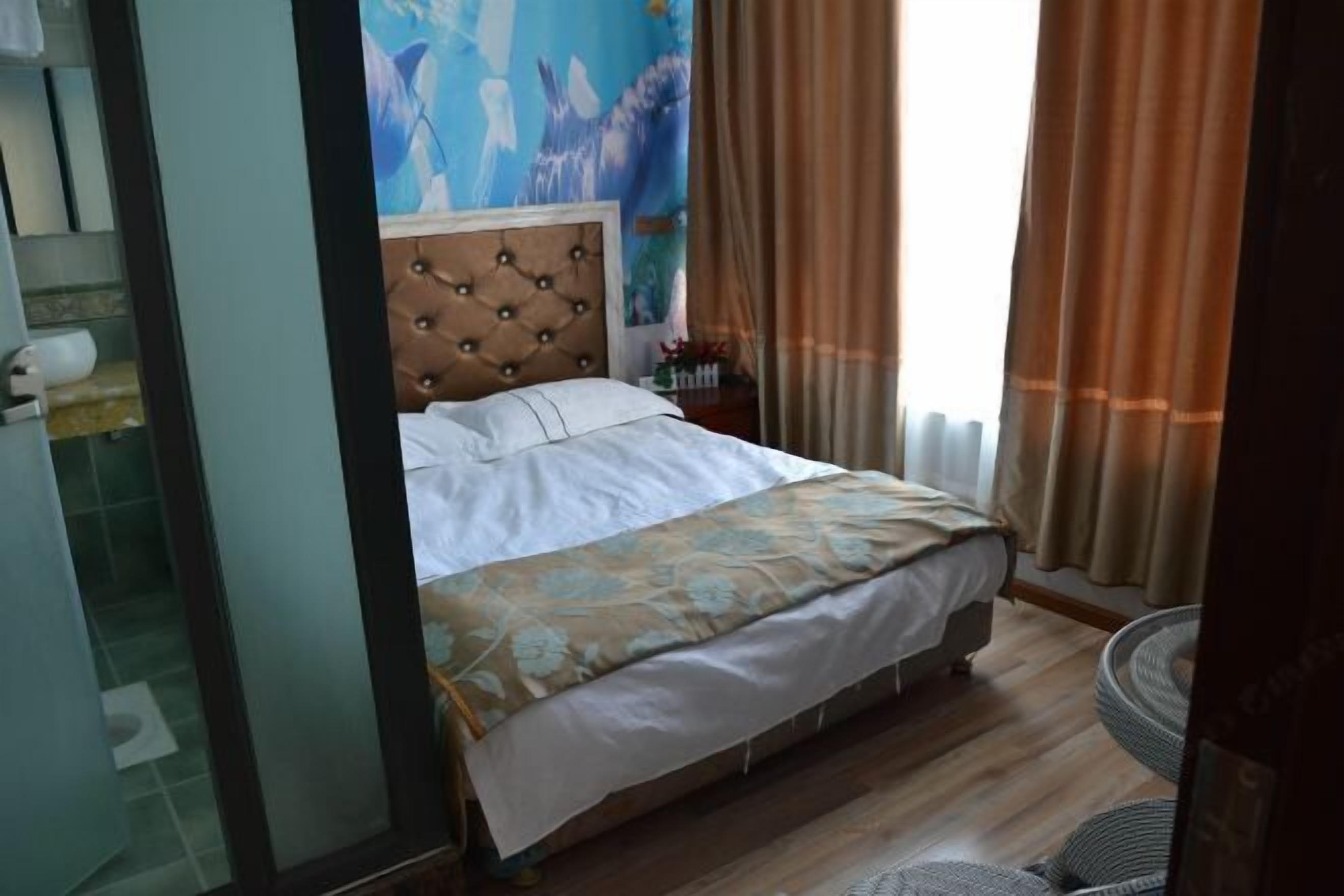 Habitació d'hotel amb un llit, un capçal, una tauleta de nit i una finestra amb cortines.