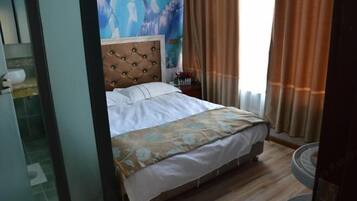 Habitació d'hotel amb un llit, un capçal, una tauleta de nit i una finestra amb cortines.