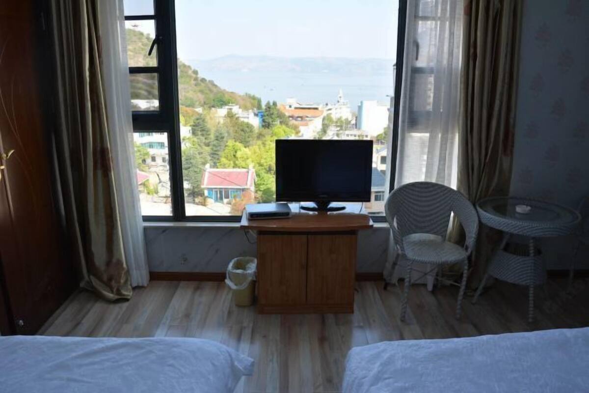 Una camera d'albergo con un letto, una scrivania con televisore, una sedia in vimini e un tavolino.