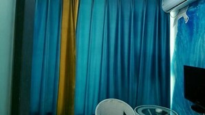 A room with a curtain, a chair, and a wall-mounted air conditioning unit. - Chengjiang Green Water Hotel (Chengjiang)