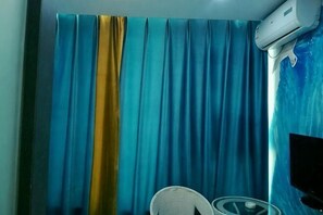 A room with a curtain, a chair, and a wall-mounted air conditioning unit. - Chengjiang Green Water Hotel (Chengjiang)