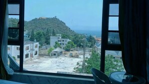 A view through a window with curtains, revealing a hillside, buildings, and a clear sky. - Chengjiang Green Water Hotel (Chengjiang)