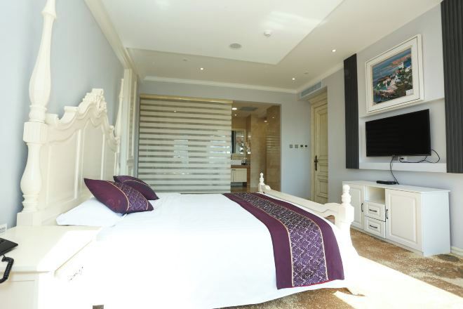 Quarto com cama grande, televisão na parede e porta deslizante para outro espaço.