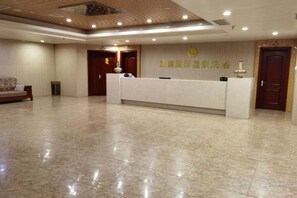 Zona de recepción de hotel con mostrador, sofá y pared con un logotipo.