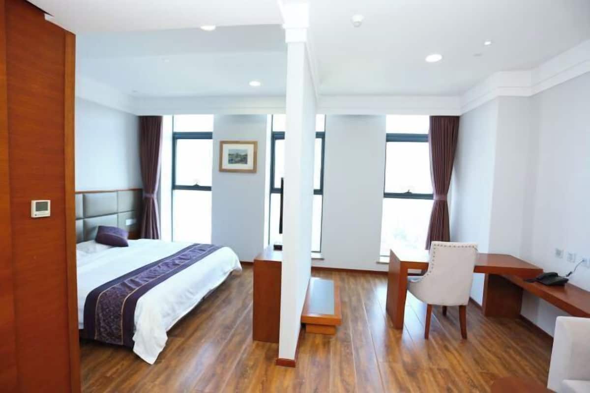 A hotel room with a bed, a desk, a chair, and large windows.