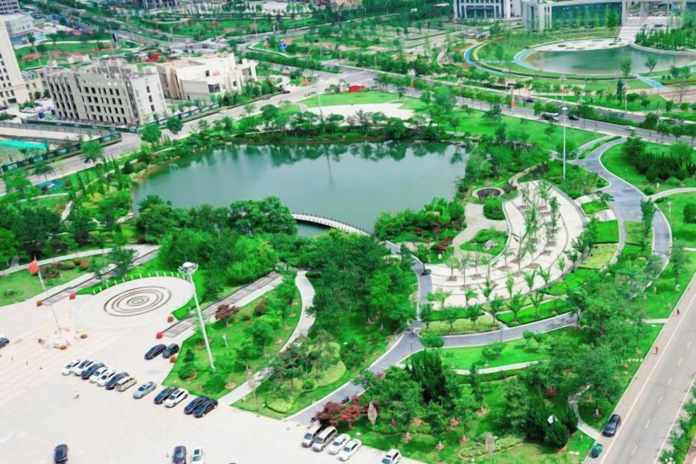 Vue aérienne d’un parc urbain avec un lac circulaire, des allées et une végétation luxuriante tout autour.