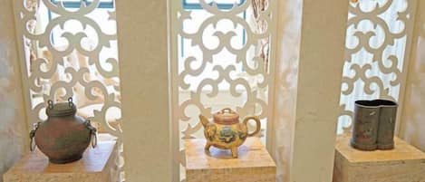 A room with a decorative screen featuring intricate patterns. There are two small tables, each with a single decorative item: a ceramic pot and a small vase.